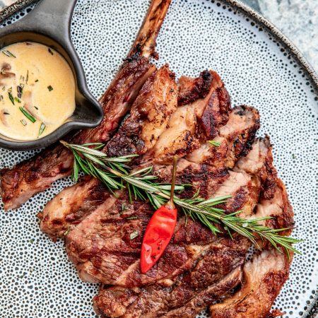 Juicy ribeye steak garnished with rosemary and chili pepper, served with creamy sauce.